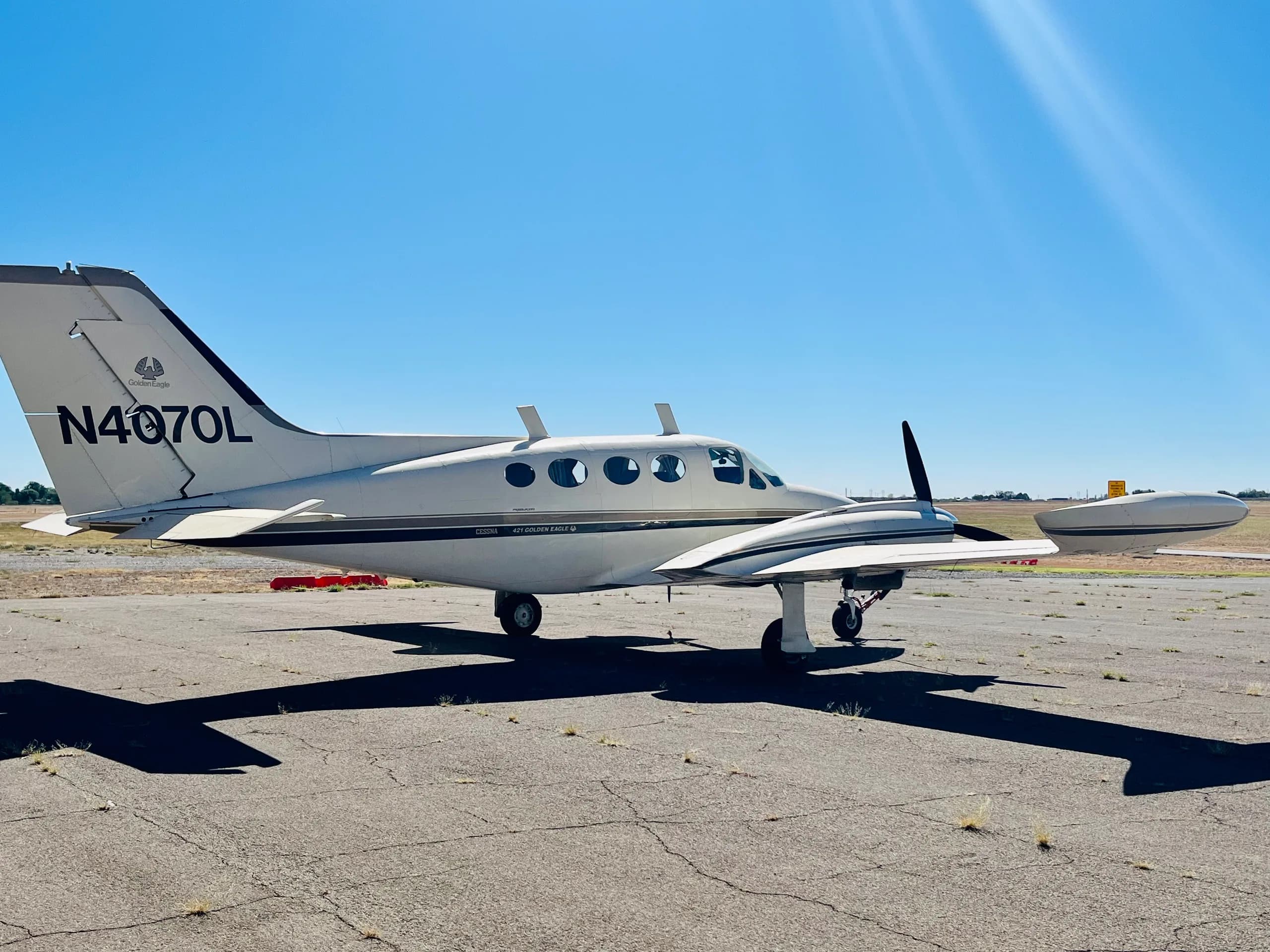 A side view of a white and gold Cessna 421 Golden Eagle (N4070L) parked on an airfield under a bright sky.