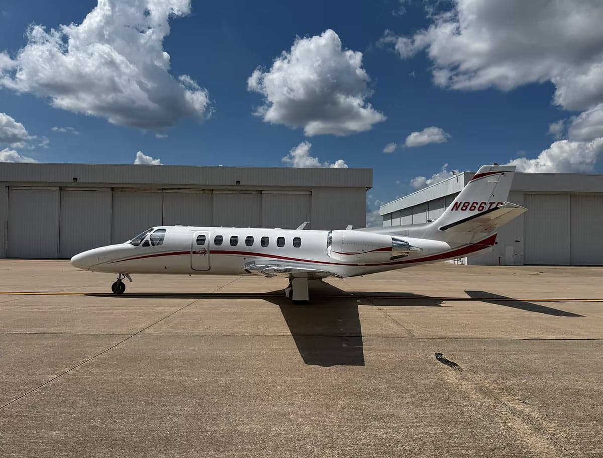 Side view of a white jet with red stripes, parked on the tarmac.