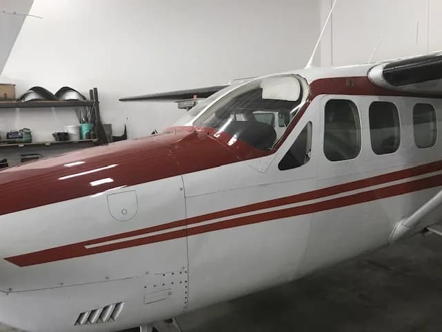 A front-side view of the cockpit and nose of a white and red Cessna 337 Skymaster in a hangar.