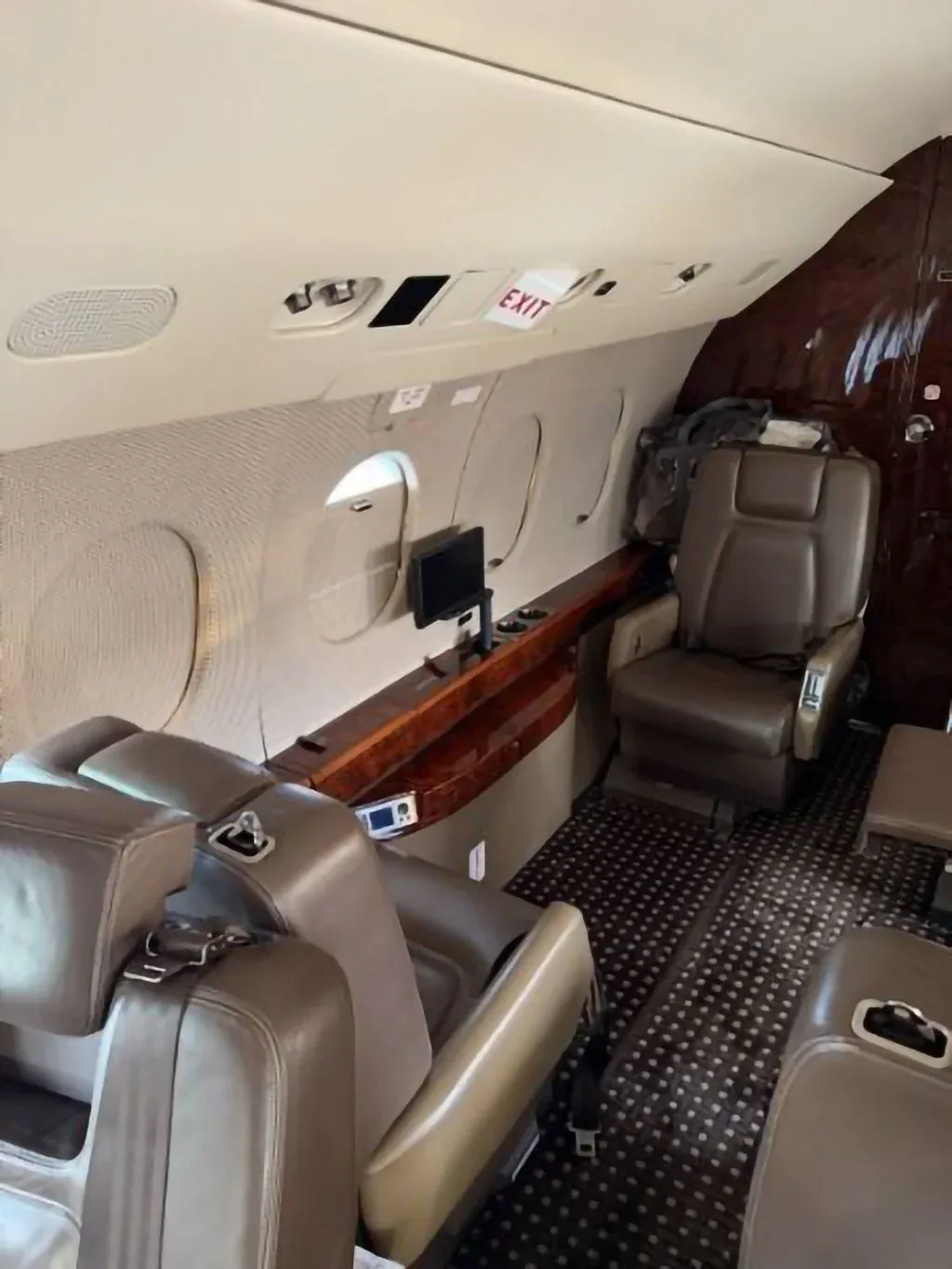 View of the aircraft cabin with brown leather seats, a side console, and an "EXIT" sign above a window.