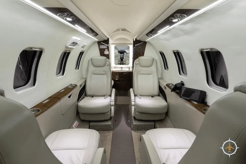 The aircraft cabin interior with light leather seats, looking towards the rear lavatory area.