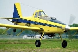 A yellow and blue Air Tractor aircraft taking off from a grassy field.