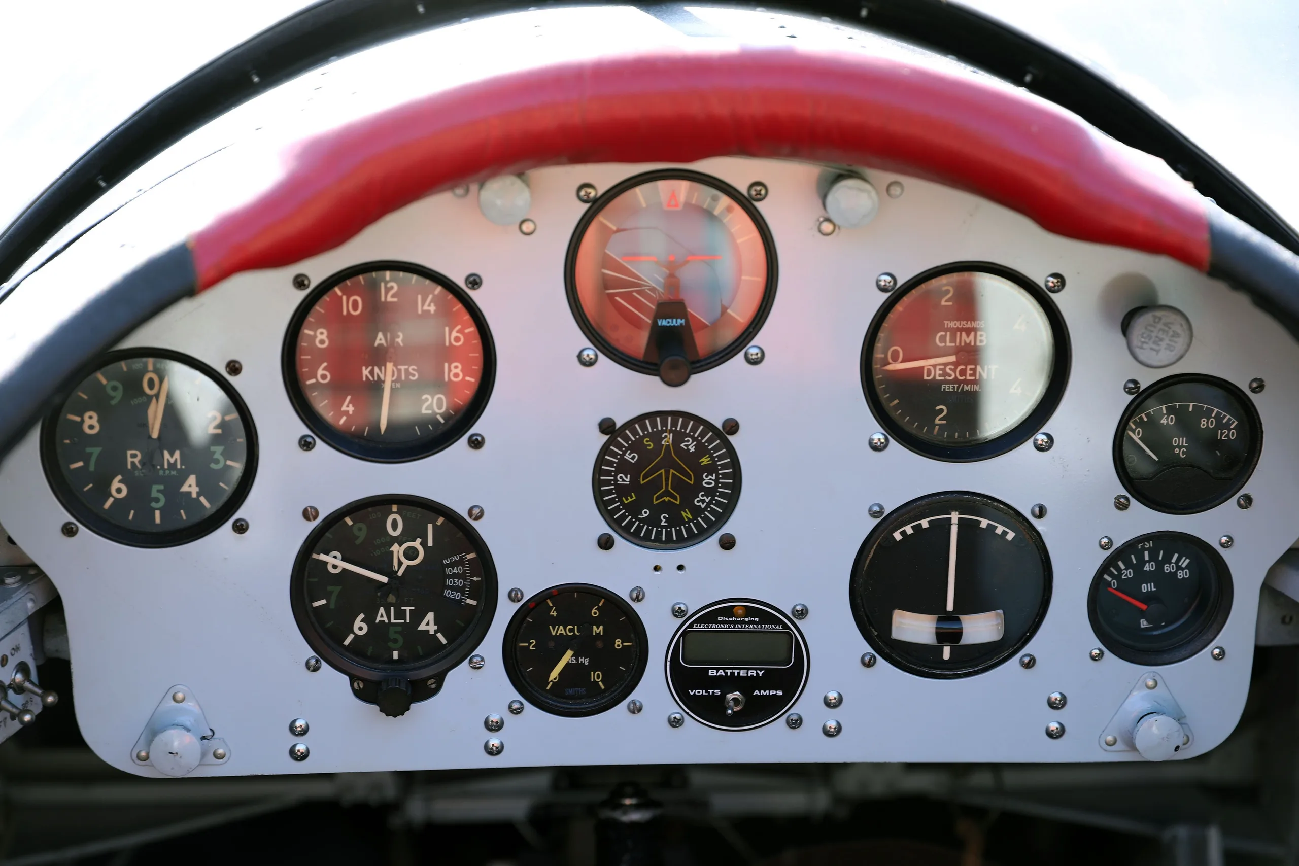 A close-up view of the vintage instrument panel of a de Havilland Canada DHC-1 Chipmunk, featuring various gauges and a red-wrapped control yoke.