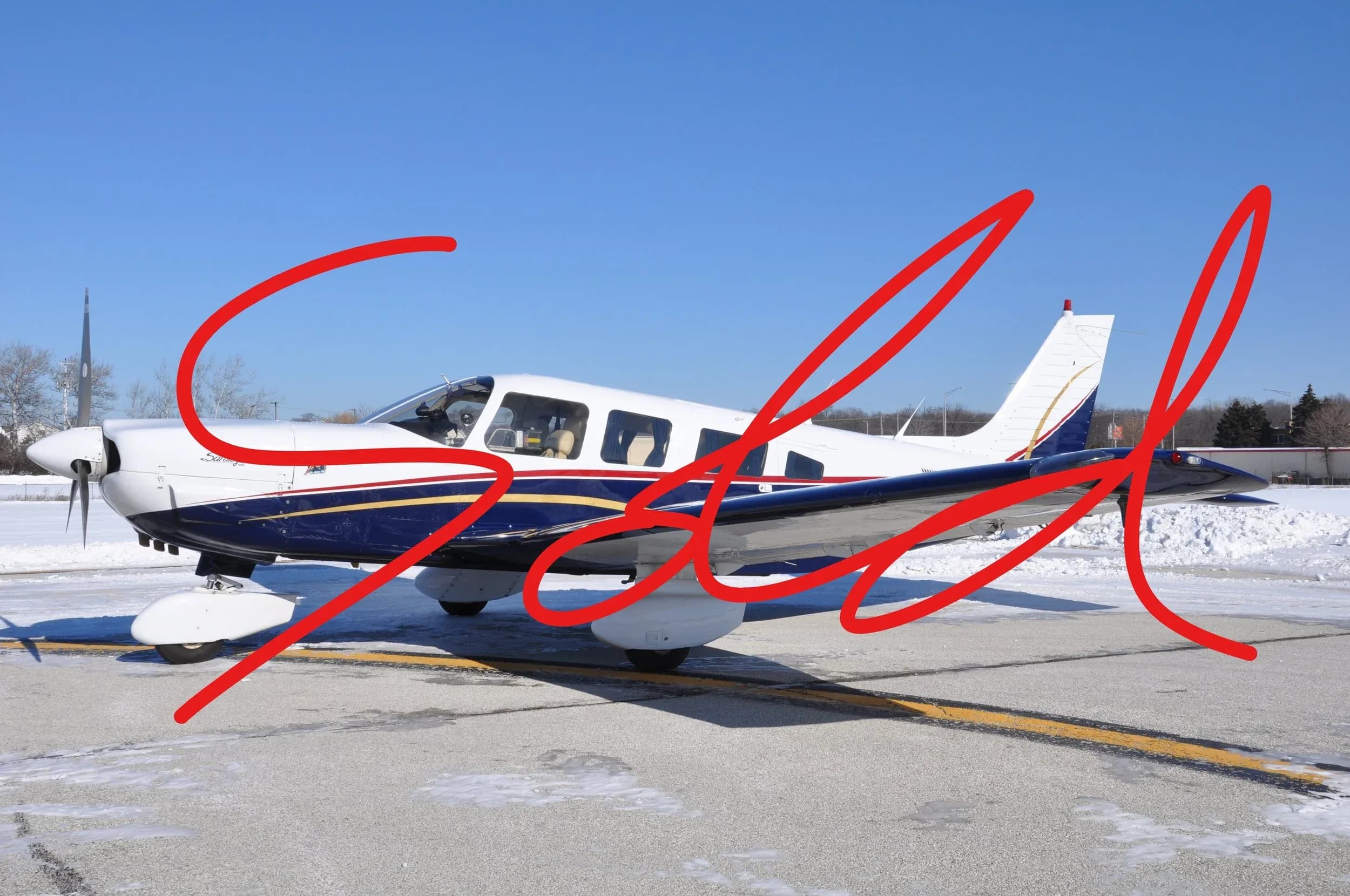 A white and blue single-engine propeller aircraft parked on a snowy tarmac under a clear blue sky.