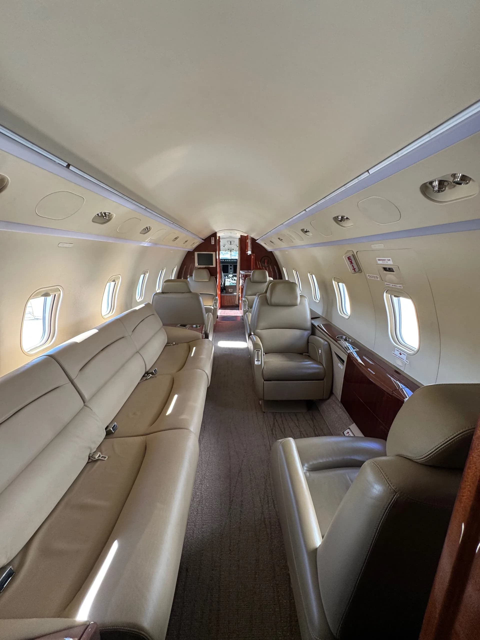 Interior view of the aircraft cabin looking forward, showing a long beige leather sofa on the left and individual seats on the right.