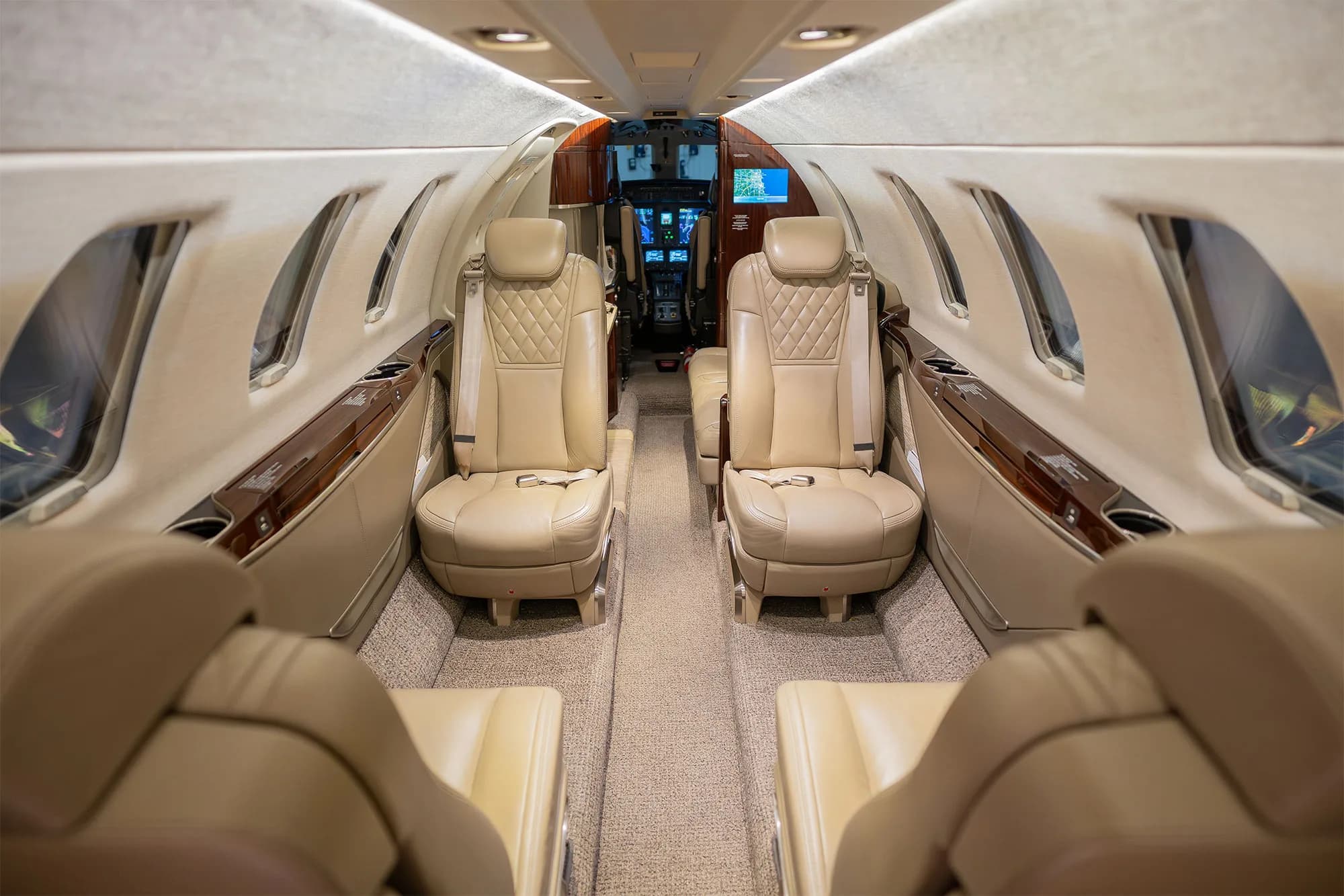 The luxurious interior cabin of a business jet with beige leather seats and overhead lighting.