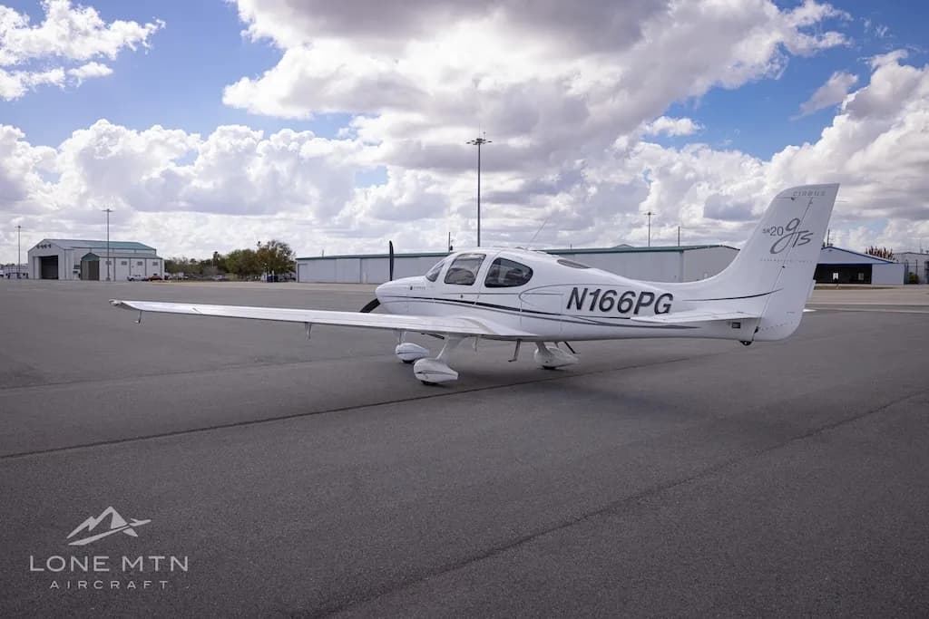 A rear-side view of the white Cirrus SR20 aircraft (N166PG) on an airport tarmac.