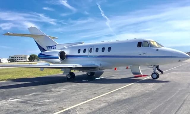 A white business jet with blue stripes (N683F) is parked on an airport tarmac under a blue sky.