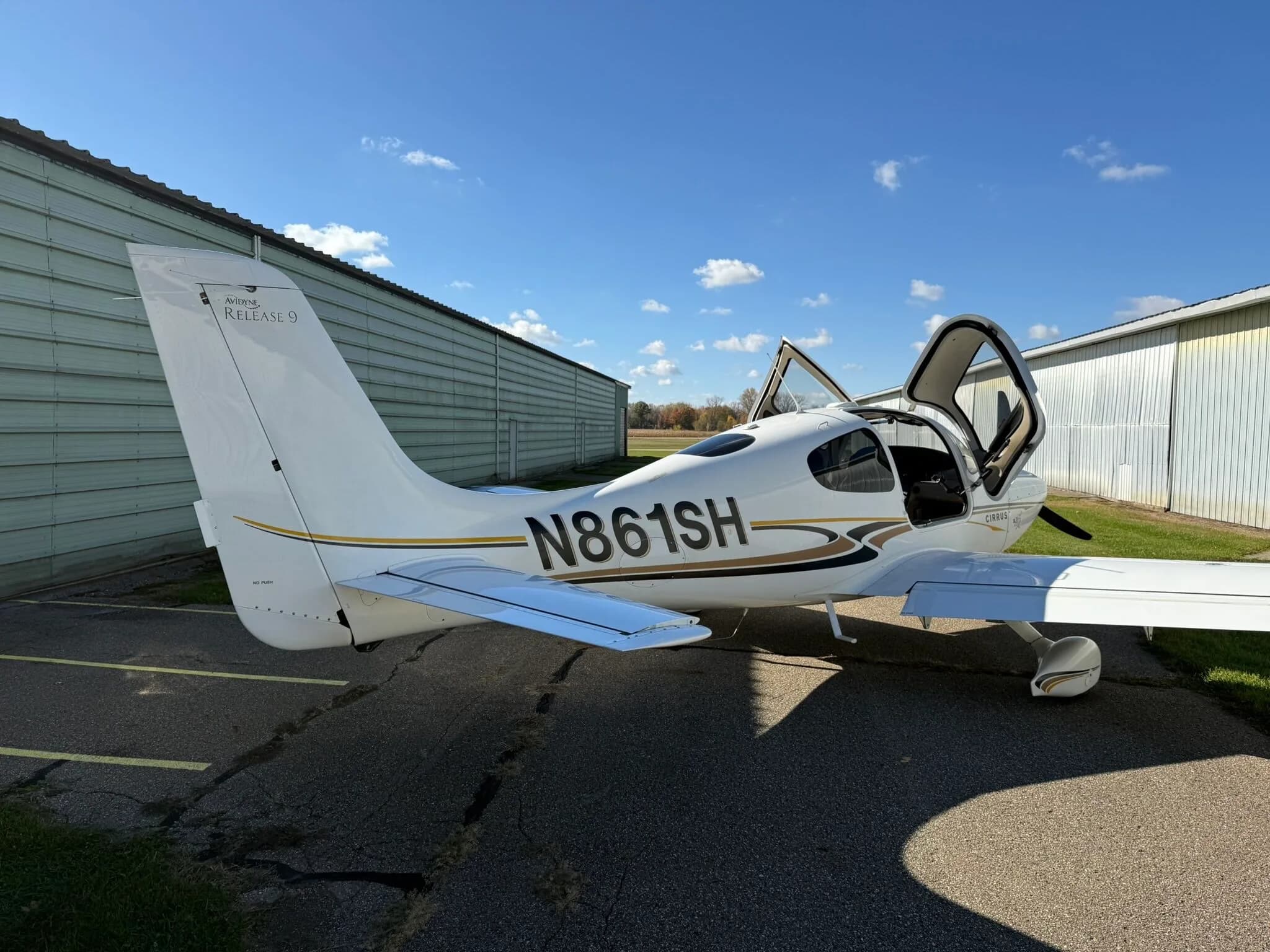 A rear-side view of a white Cirrus SR20 aircraft, registration N861SH, with its doors open, parked on an asphalt ramp.