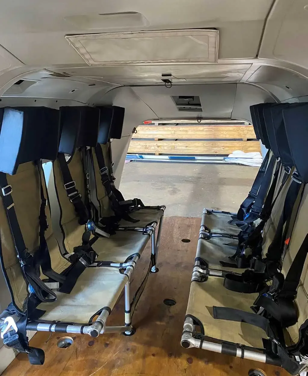The interior cabin of a helicopter with two rows of tan fabric seats with black harnesses.