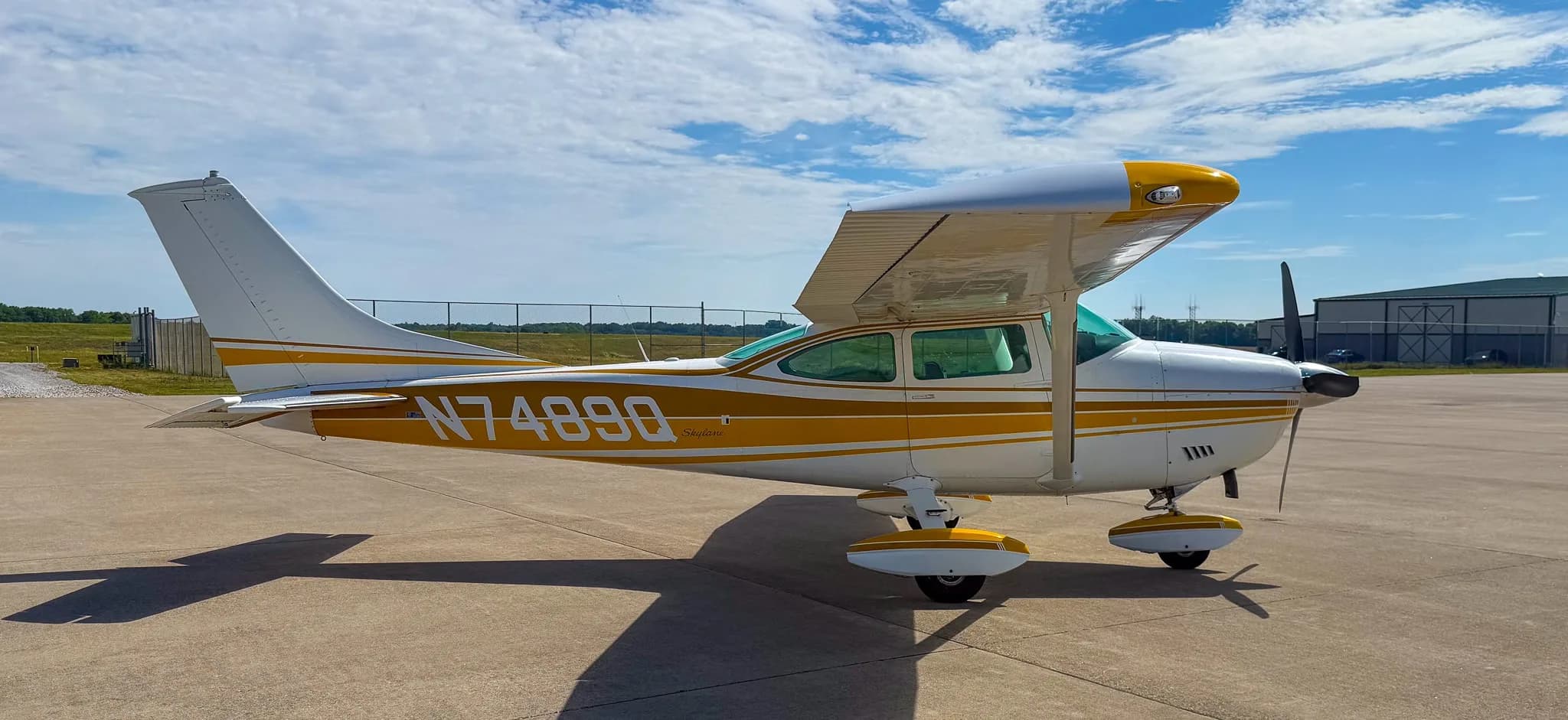 A white and gold Cessna Skylane N7489Q is parked on an airfield tarmac, viewed from the left side.