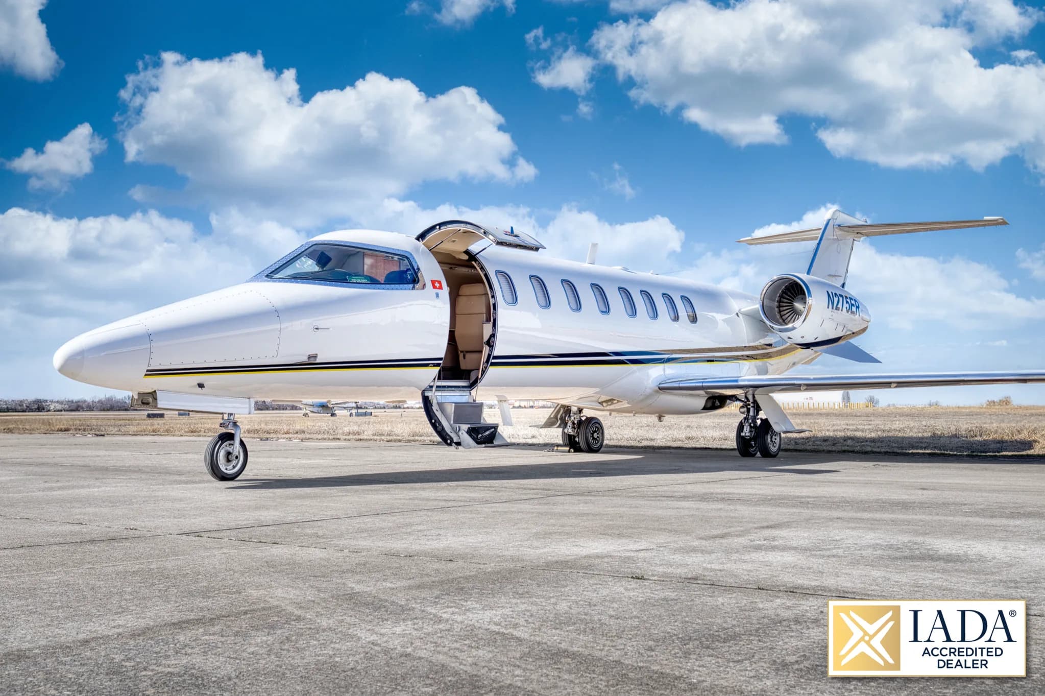A white Learjet 60 (N275ER) with a black and yellow stripe, parked on a tarmac with its main cabin door open.