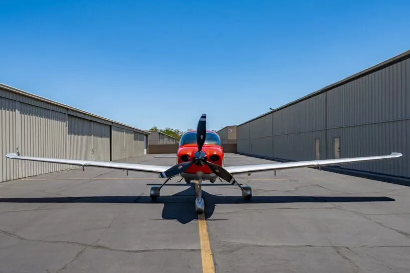 Front view of a red and silver Cirrus SR22T aircraft (N566TT) parked between hangars.