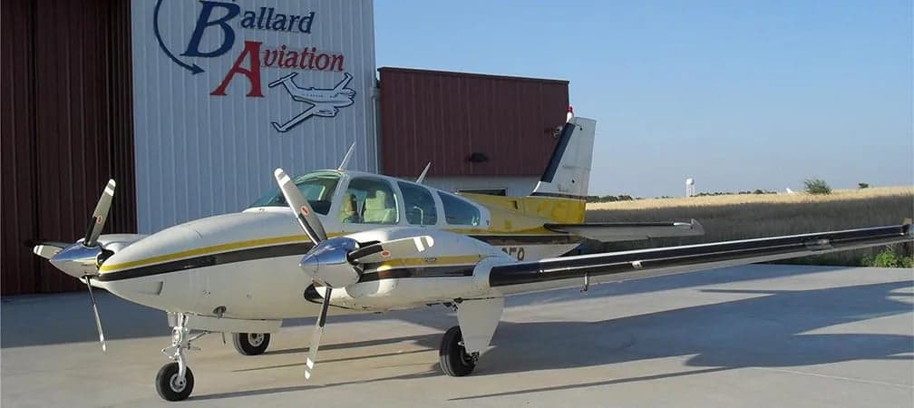 A Beechcraft Baron sits on the tarmac in front of a hangar.