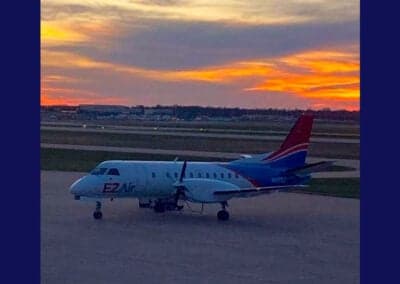 Side view of an EZ Air Beechcraft 1900 aircraft parked on the tarmac at sunset.