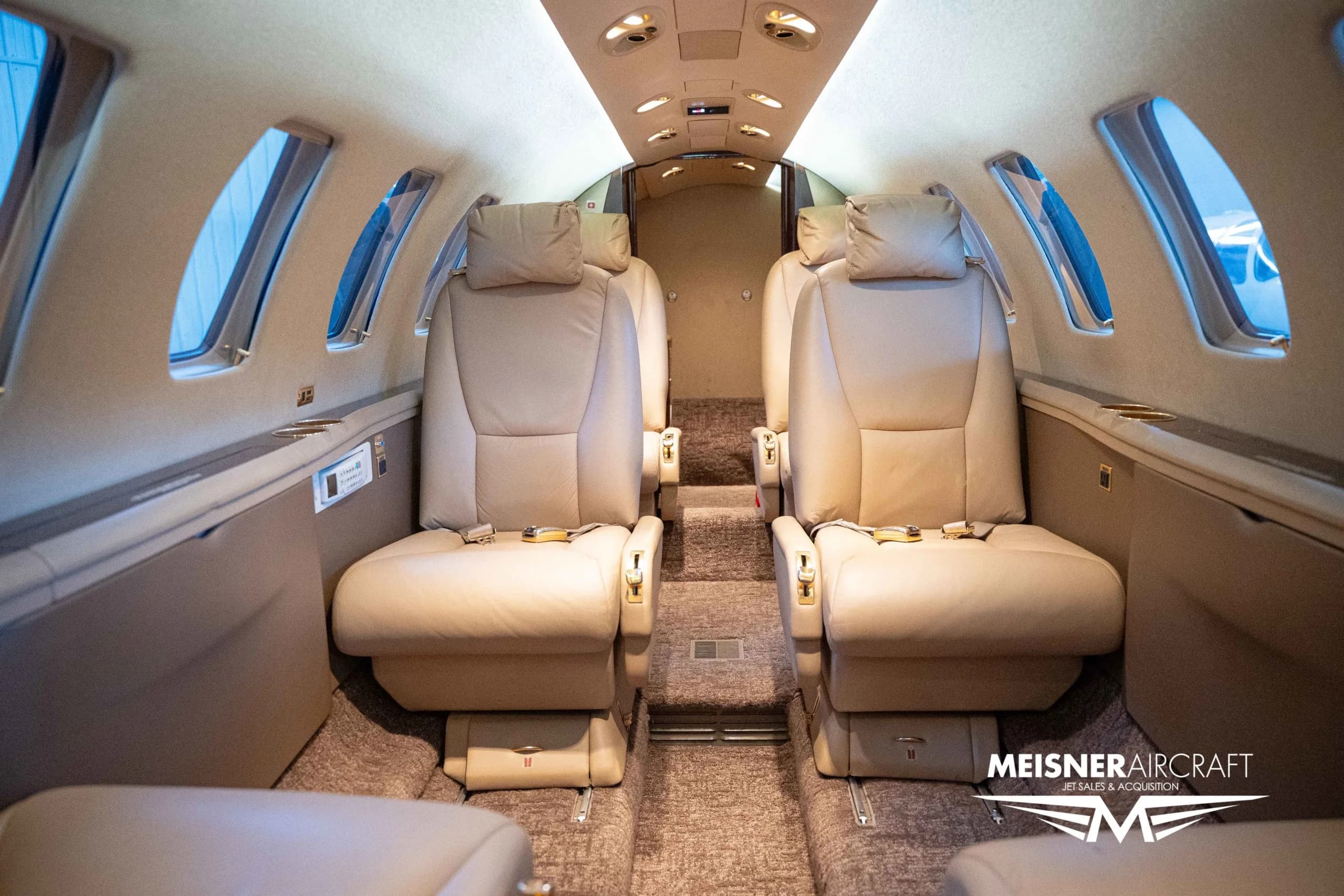 The interior cabin of a private jet, featuring beige leather seats, looking towards the rear of the aircraft.
