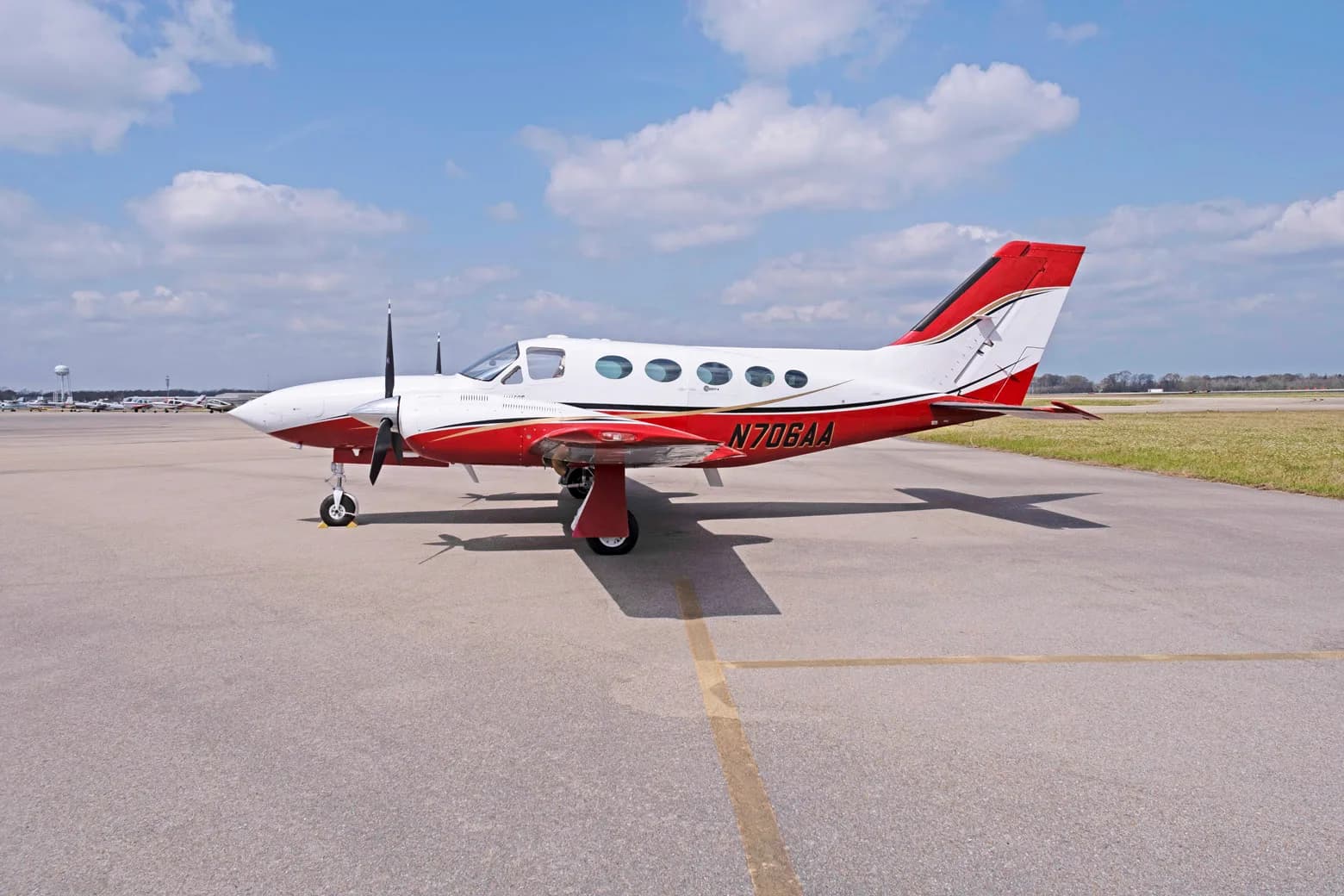 A side view of a white and red Cessna 421C Golden Eagle with registration N706AA parked on an airfield.