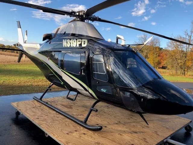A black and grey helicopter with registration N319PD parked on a wooden pallet outdoors.