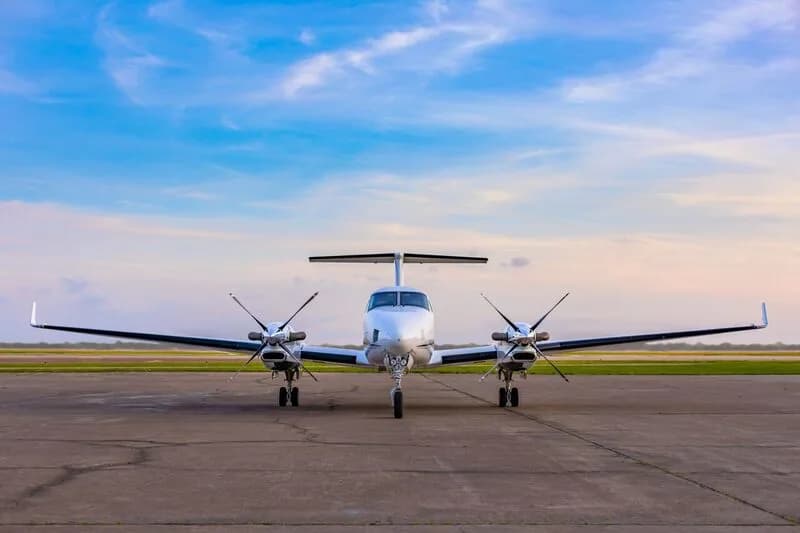 A white Beechcraft King Air 350i with twin propellers is parked head-on on an airfield.