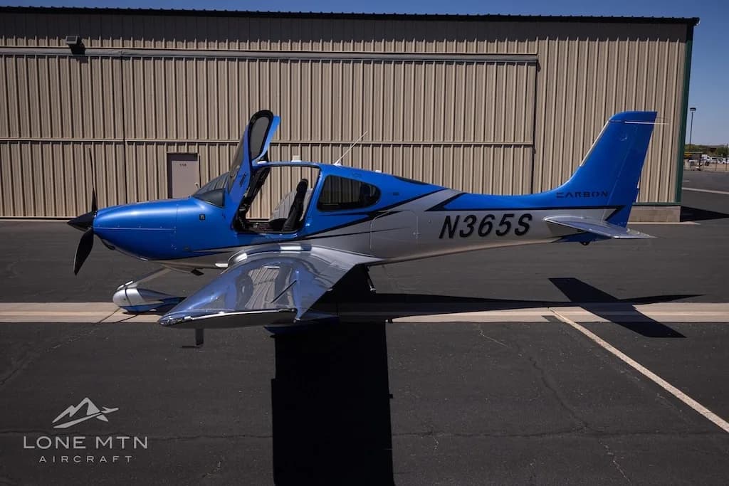 A side view of the blue and silver Cirrus SR22 aircraft, N365S, with its doors open, parked on an asphalt ramp.