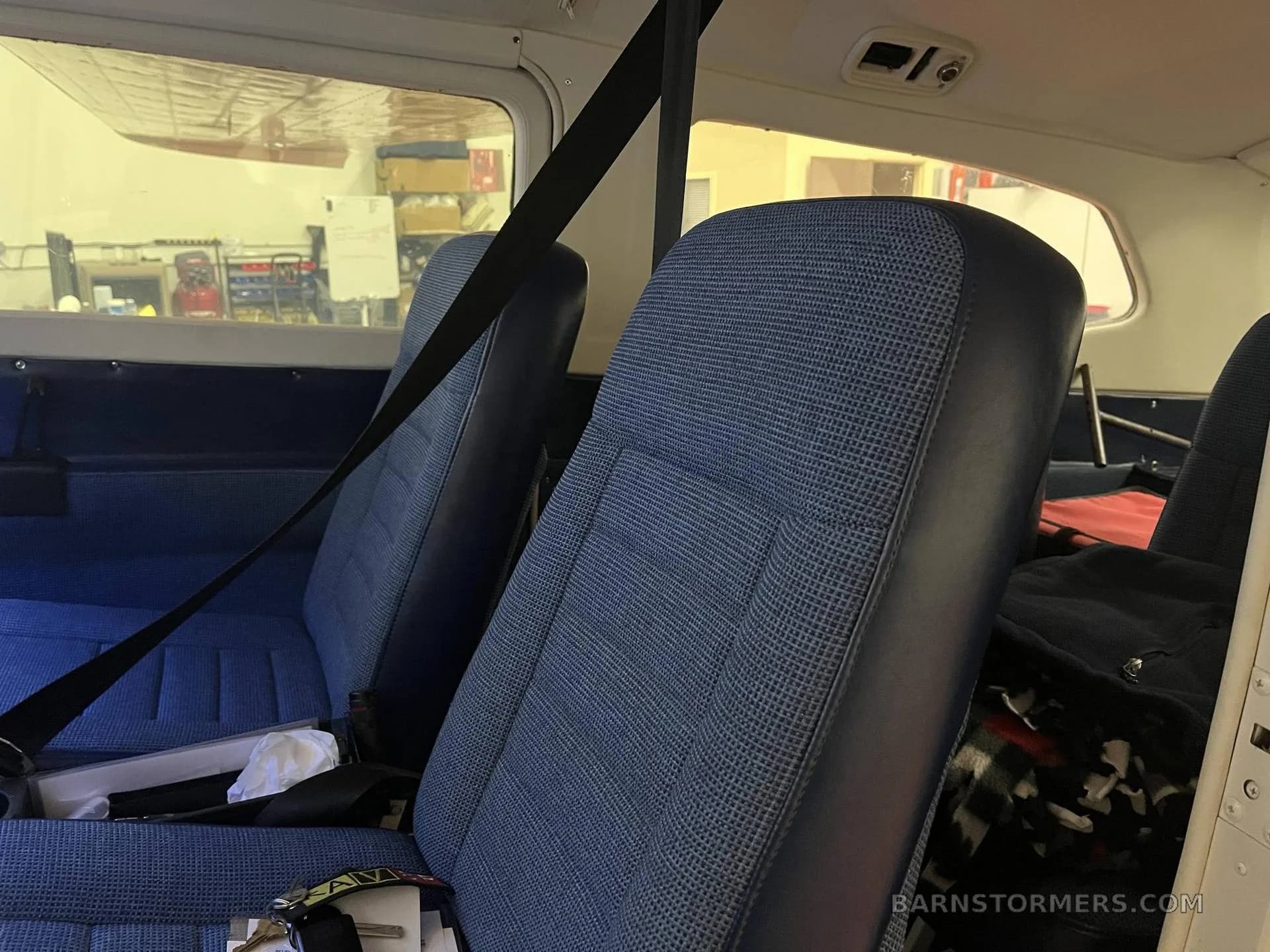 The blue fabric and vinyl interior seats of an aircraft cabin, with a view of a hangar through the window.