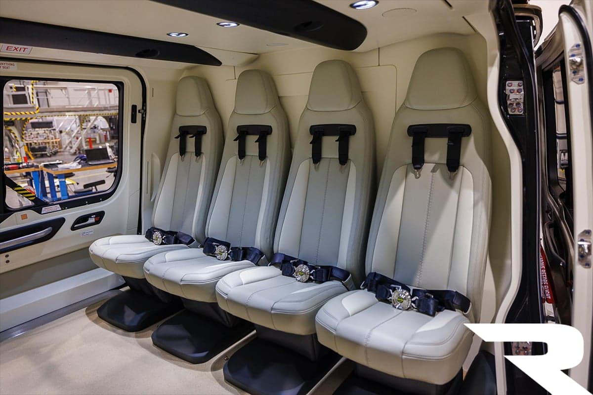 A row of four light grey passenger seats with dark seatbelts inside an Airbus H160 helicopter cabin.
