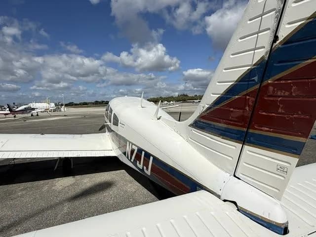 A rear-side view of the white Piper Cherokee aircraft N7JJ, highlighting its tail section with blue and red stripes.