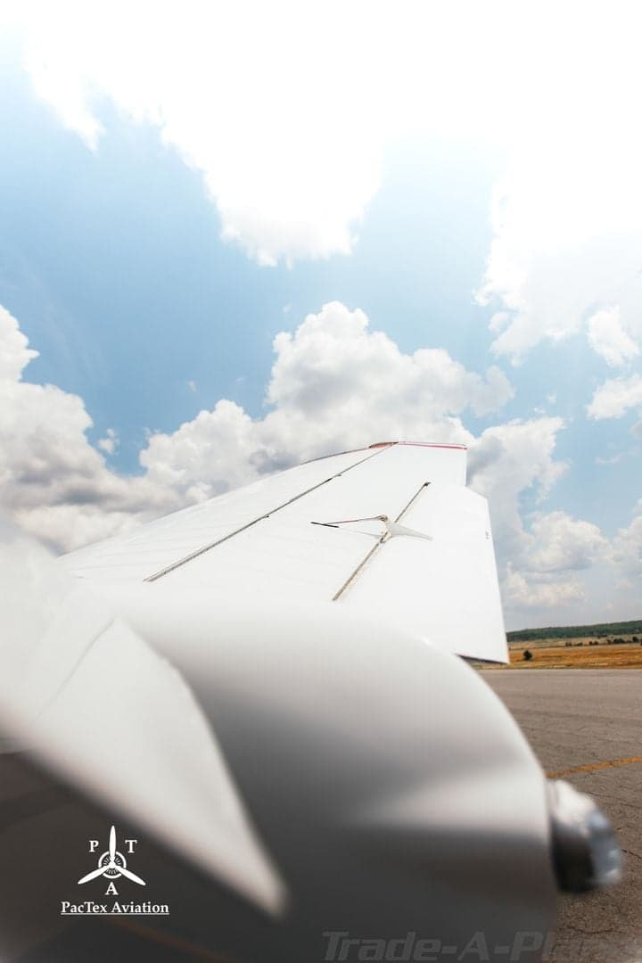Upward view of the wing of a white aircraft against a bright blue sky with clouds.