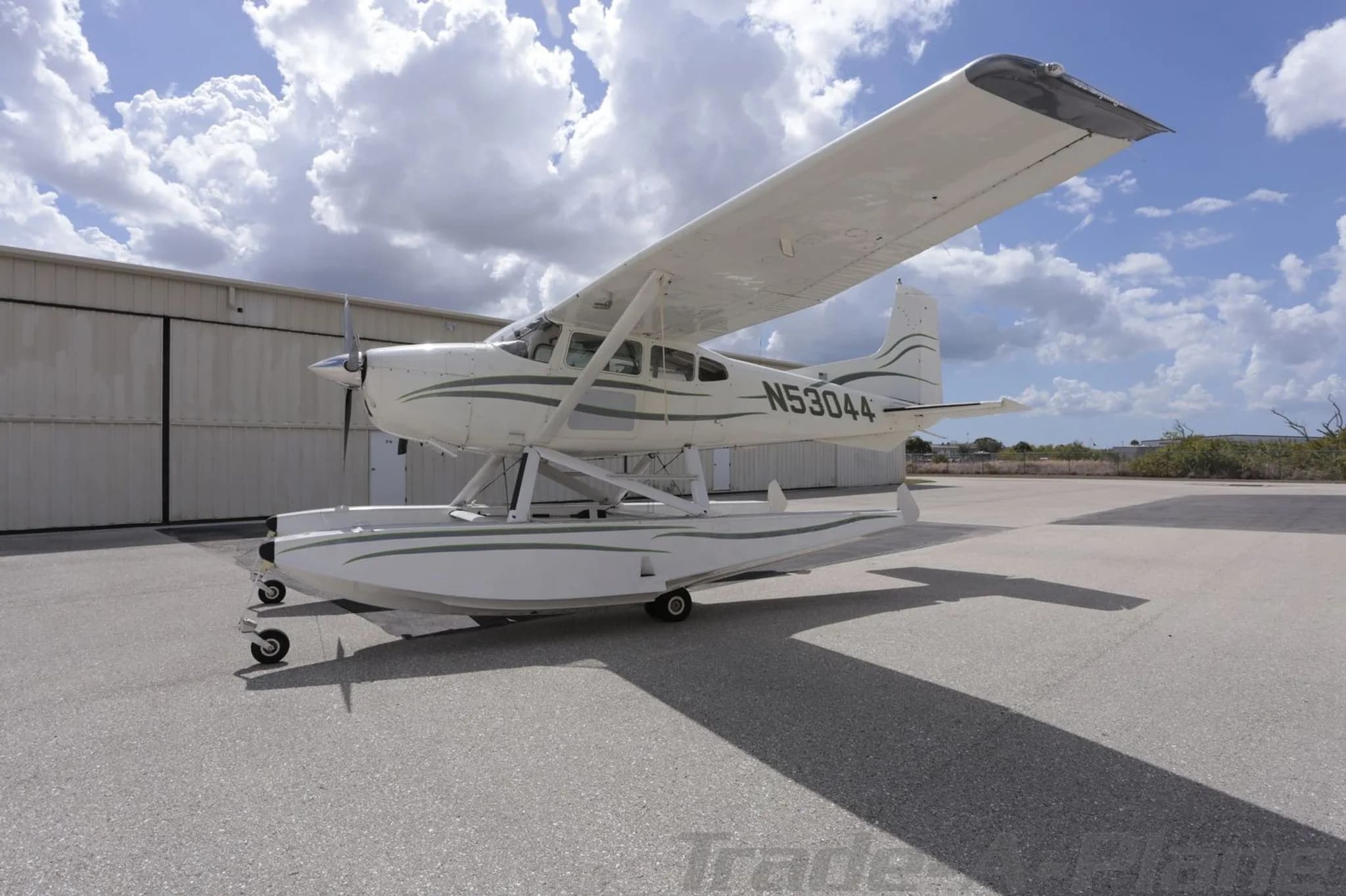A white Cessna 180 Skywagon seaplane with green stripes, registration N53044, parked on an asphalt ramp.