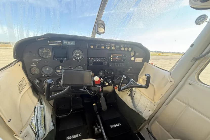 A wide view of the cockpit of a Cessna 172, showing the instrument panel, yokes, and pedals.