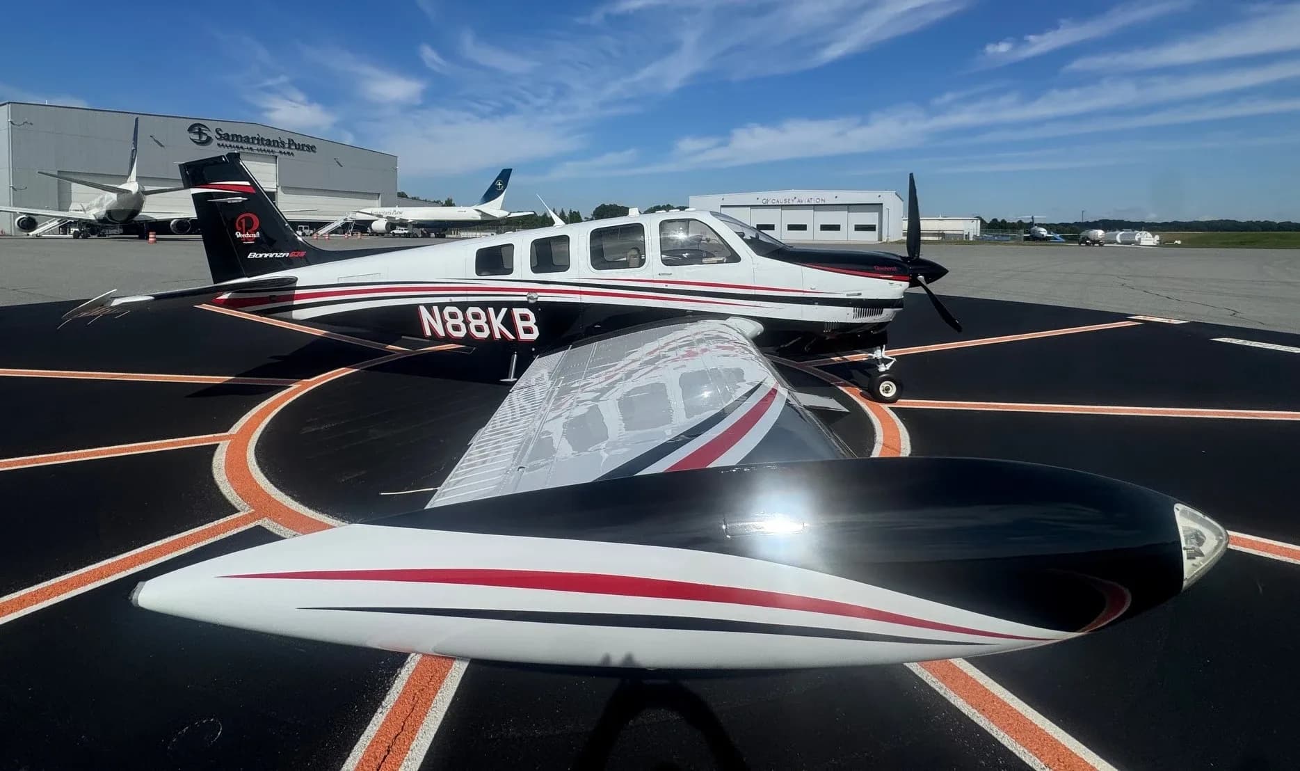 A low-angle view of a white and black Beechcraft Bonanza with red stripes, tail number N88KB, on an airport tarmac.