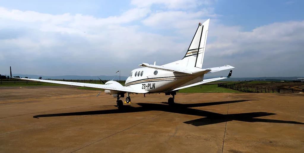 A white Beechcraft King Air C90GTx aircraft with registration ZS-PLN, seen from the rear, parked on a tarmac with long shadows.