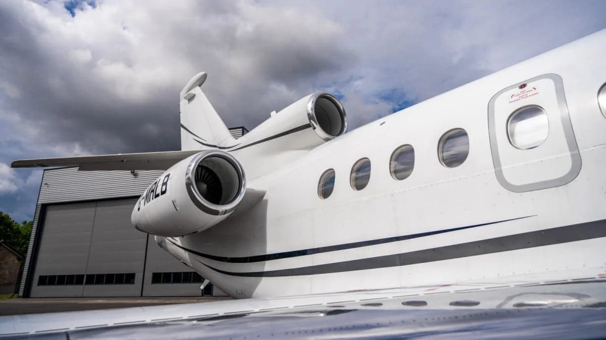 A white Dassault Falcon 7X business jet parked on the tarmac in front of a hangar.