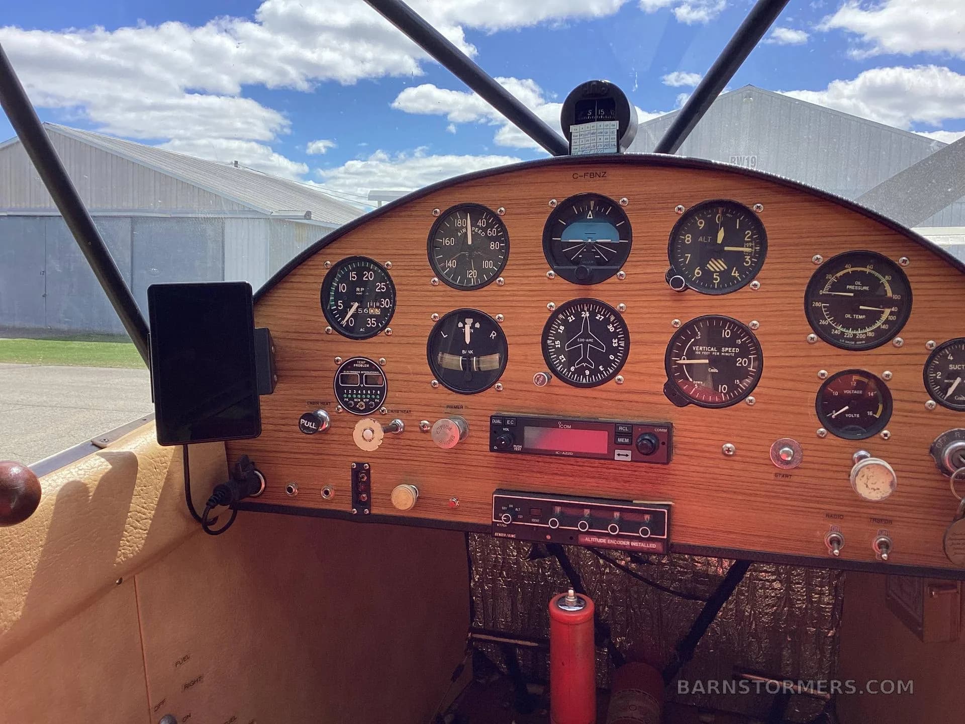 The aircraft's cockpit features a wooden instrument panel with various analog gauges and a radio, viewed from the pilot's seat.