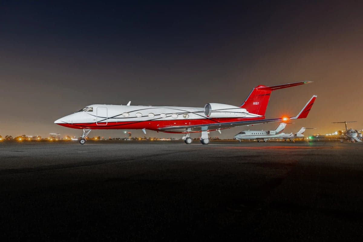 Side view of a red and white Gulfstream G550 on the tarmac at night.