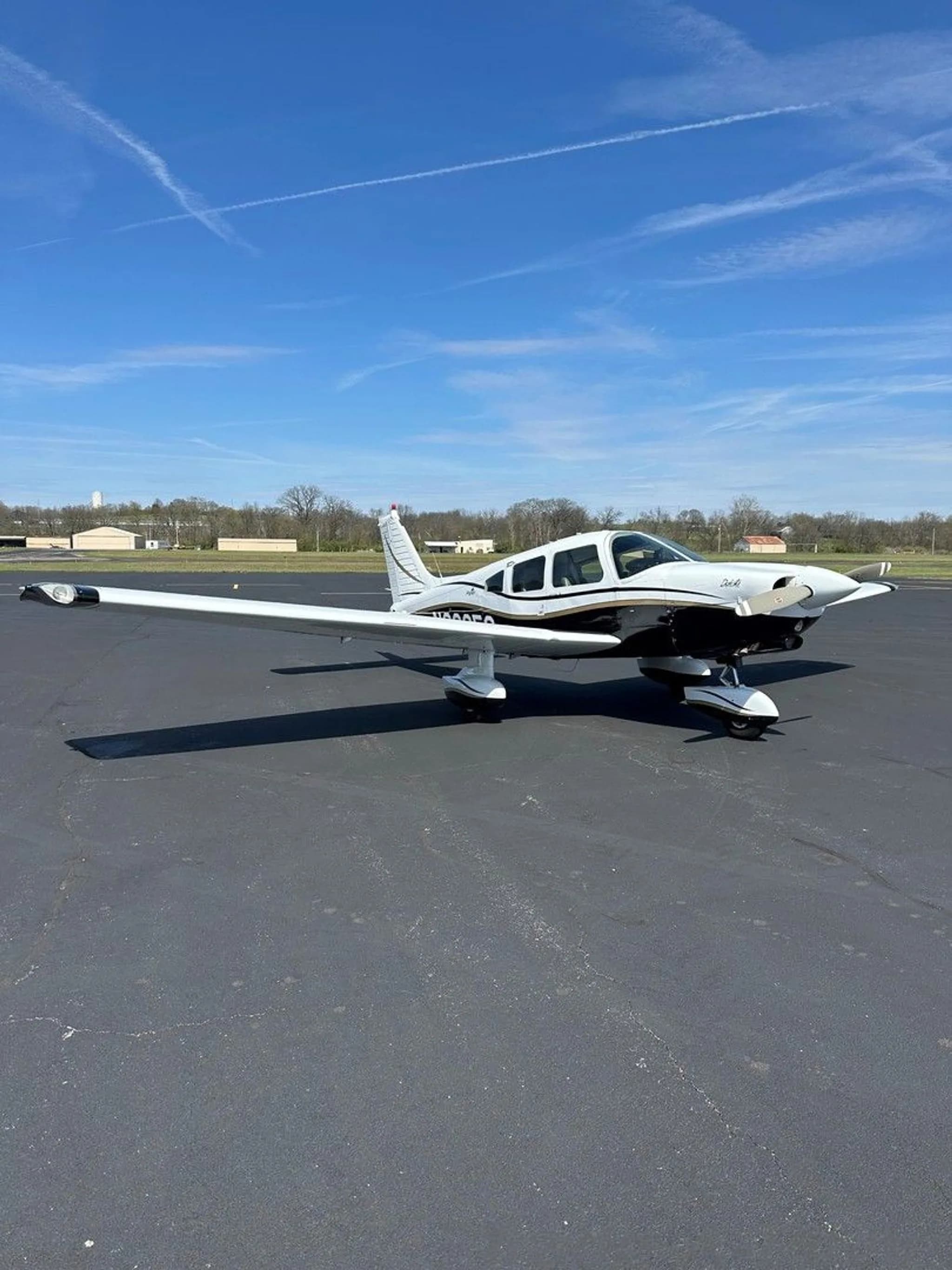 A white and black Piper aircraft with gold trim, registration N2235C, parked on an asphalt ramp under a blue sky.