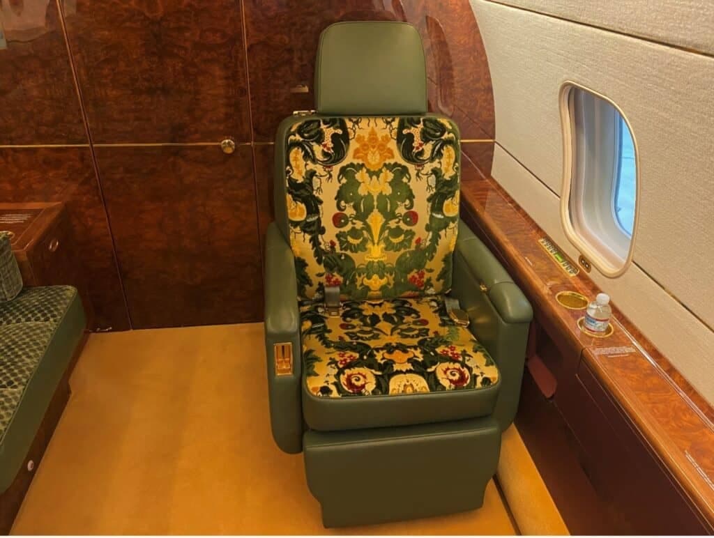 A single green leather seat with ornate green and gold patterned upholstery inside the luxurious cabin of a Bombardier Challenger 604.