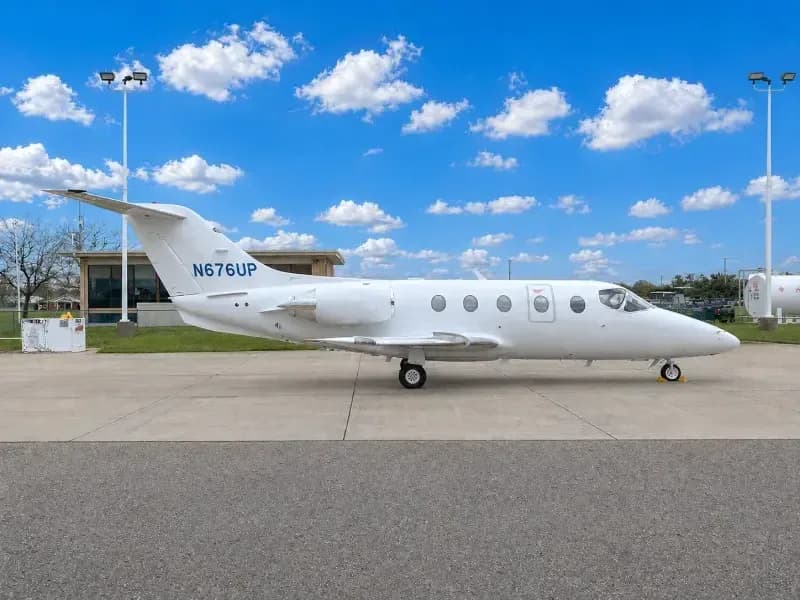 A white private jet, N676UP, is parked on an airport tarmac under a blue sky with white clouds.