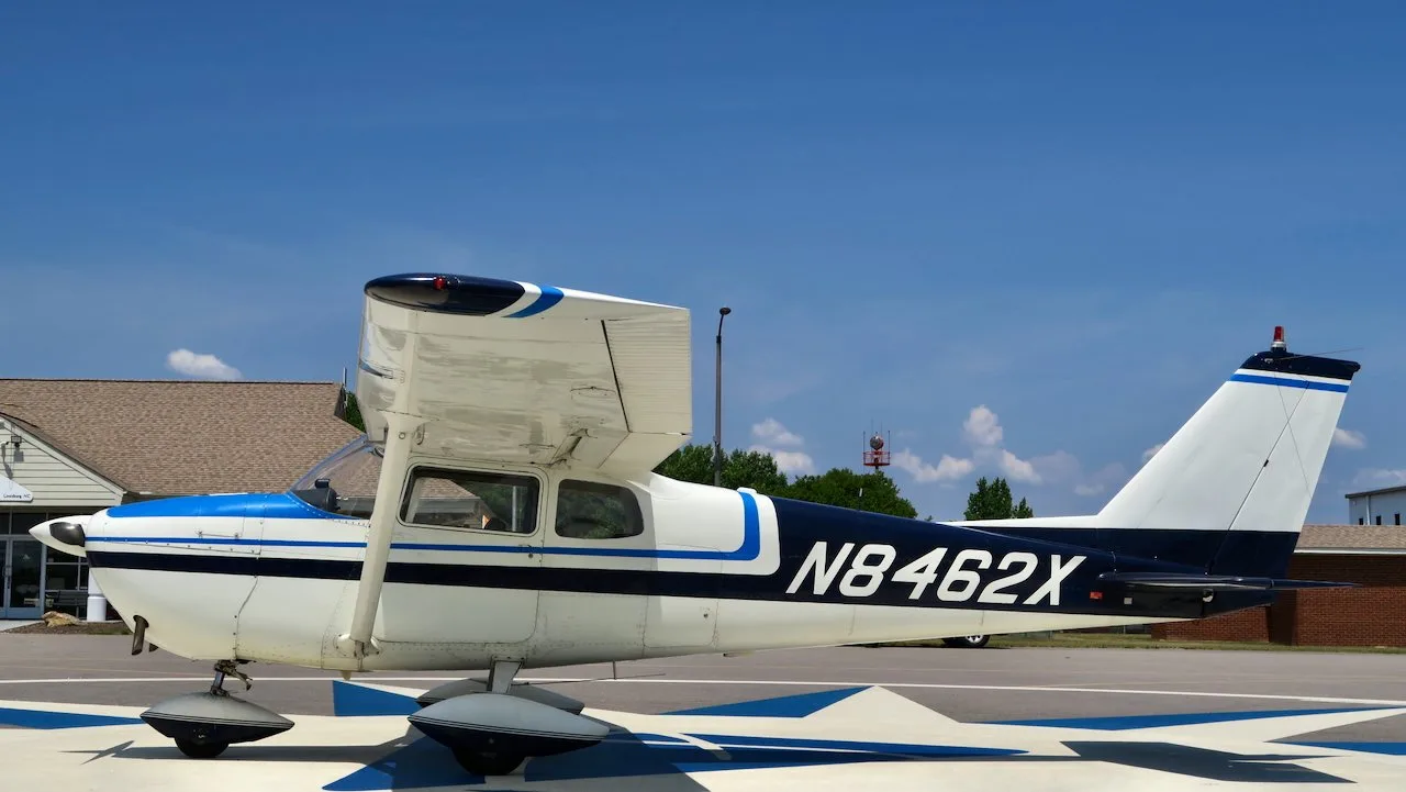 A side view of a white Cessna 172 with blue and black stripes, N8462X, parked on an airfield.