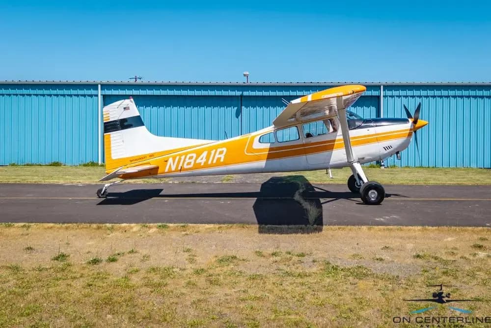 A side profile view of a white and orange Cessna 185 Skywagon (N1841R) parked on an asphalt ramp.