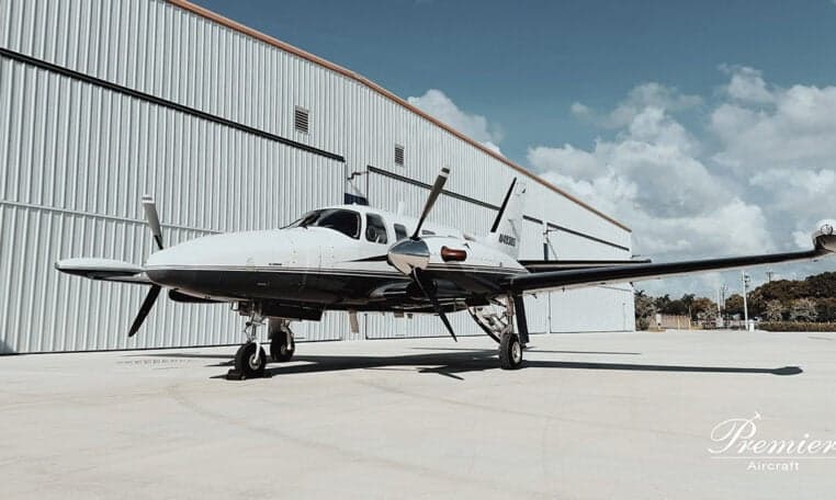 A twin-engine aircraft, N4938S, parked in front of a hangar on a sunny day.