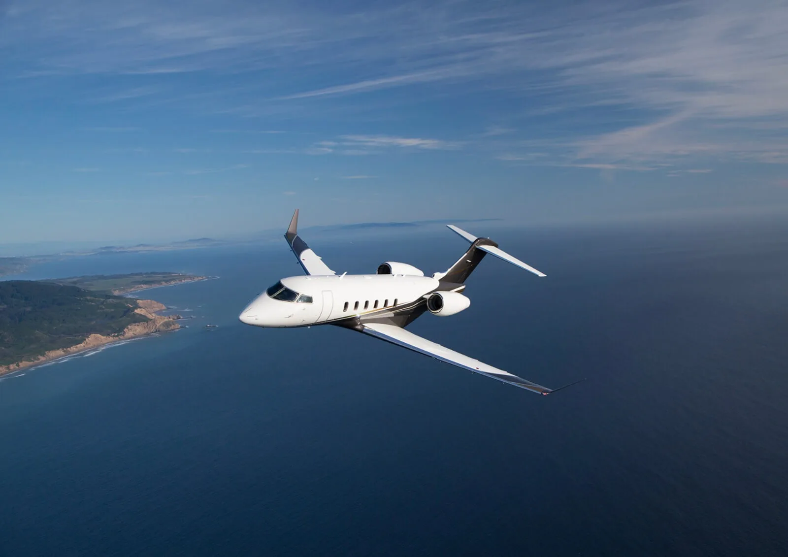 A white and gray jet flies over the ocean.