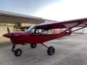 A red Cubcrafters aircraft is parked outside a hangar.