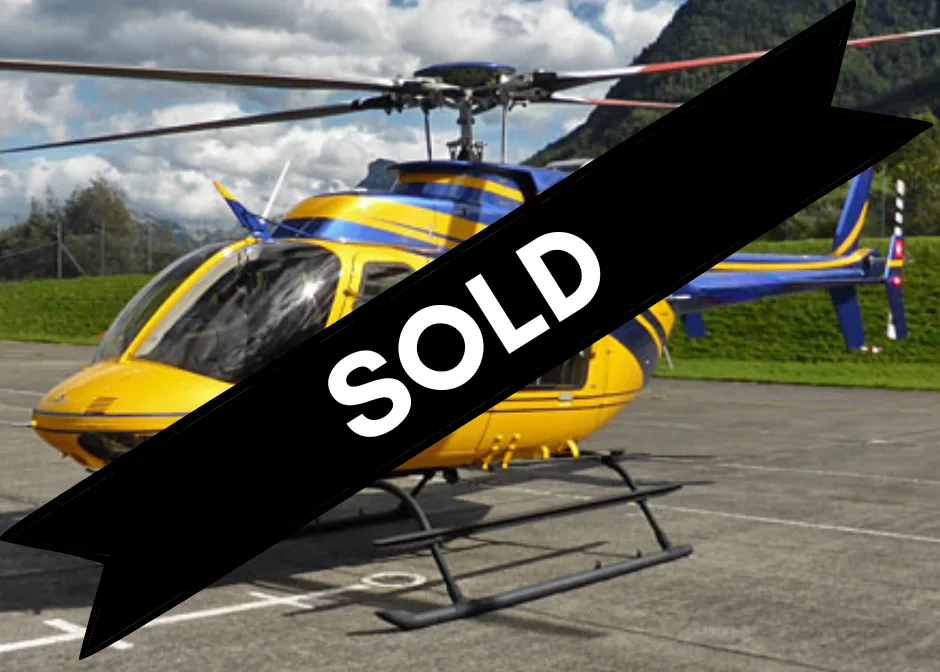 A yellow and blue helicopter, possibly an Eurocopter AS350, parked on a tarmac with mountains in the background.