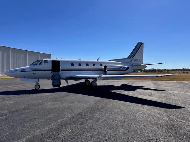 A full side view of the N700JC business jet with its airstair door open, showing its white fuselage with blue and gold stripes.