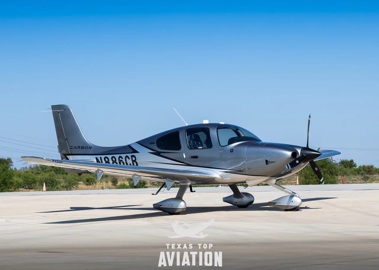 A three-quarter front view of a silver and grey Cirrus SR22 aircraft with registration N886CB on an airfield.