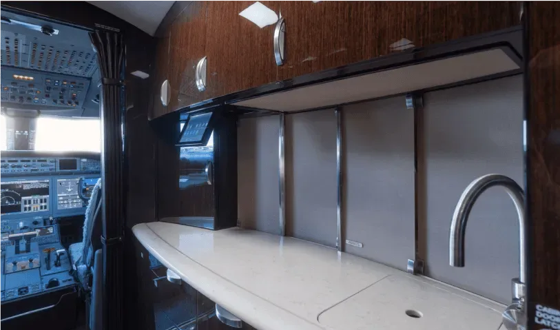 A view of the aircraft's galley area with a sink and storage, with the cockpit visible through an open doorway.