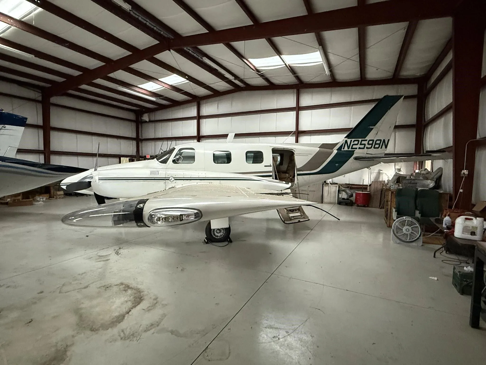 A white twin-engine Piper Navajo aircraft with green and brown stripes, seen from the left side with the passenger door open in a hangar.