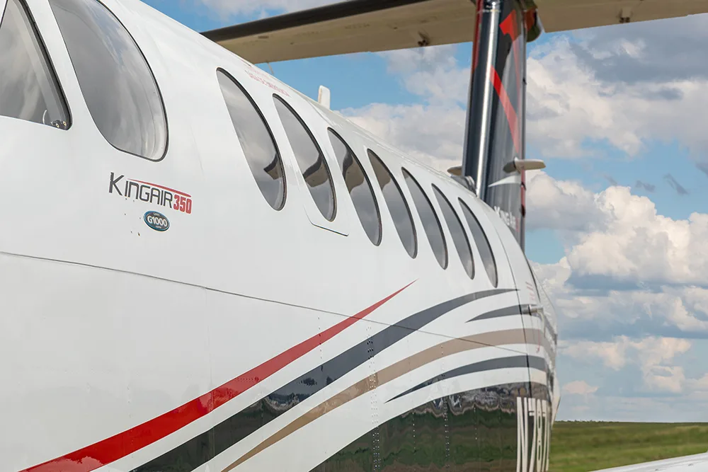 A close-up view of the white fuselage of a King Air 350 aircraft with black, red, and gold stripes, showing the tail section.