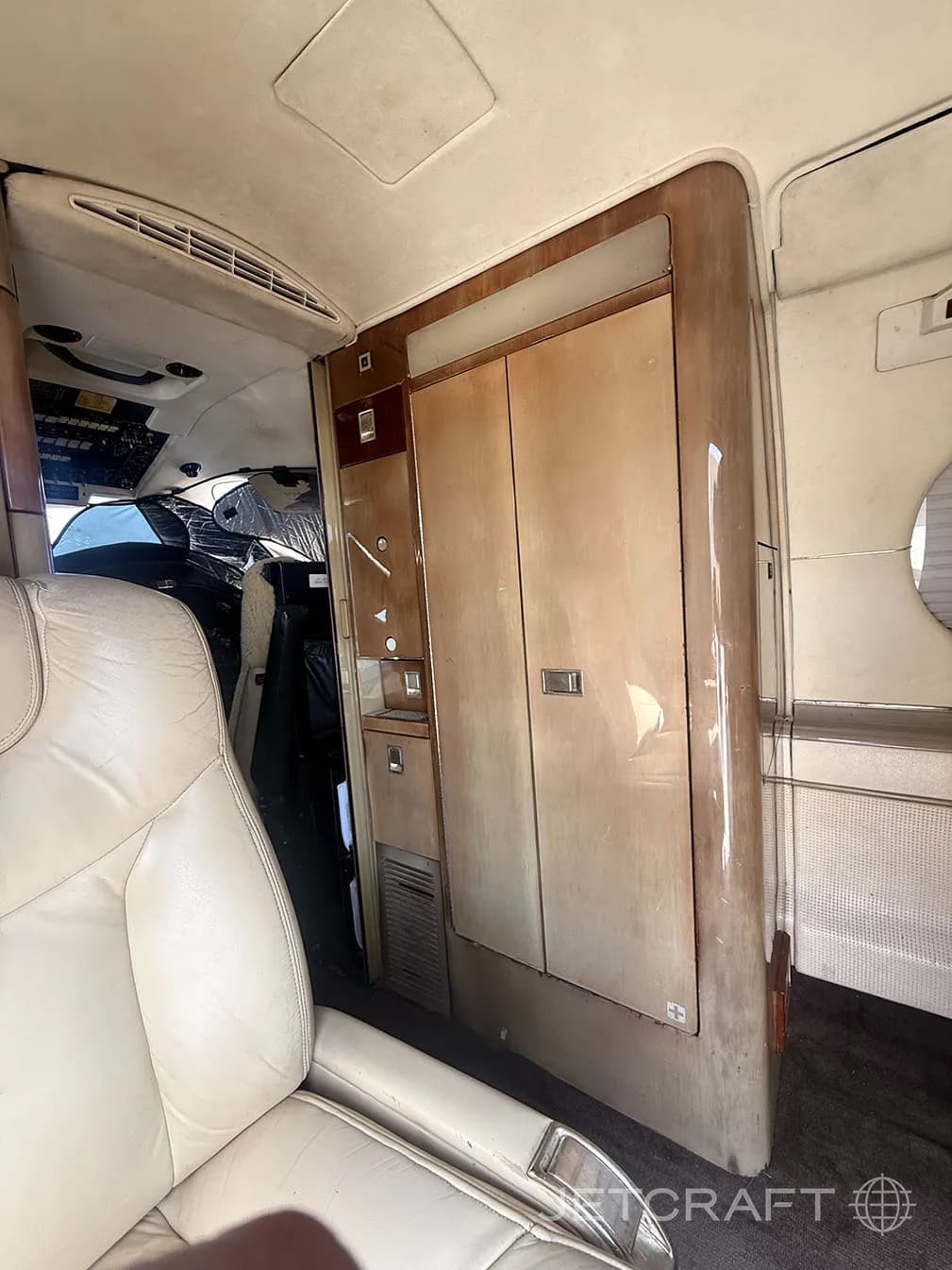 A wooden cabinet and part of a tan leather seat in the interior of a private jet.